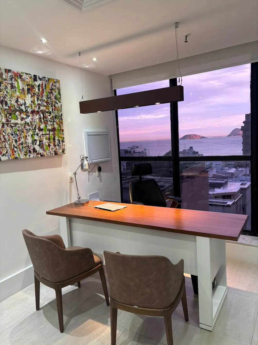 Sala de atendimento do consultório, com mesa, duas cadeiras e janela ampla