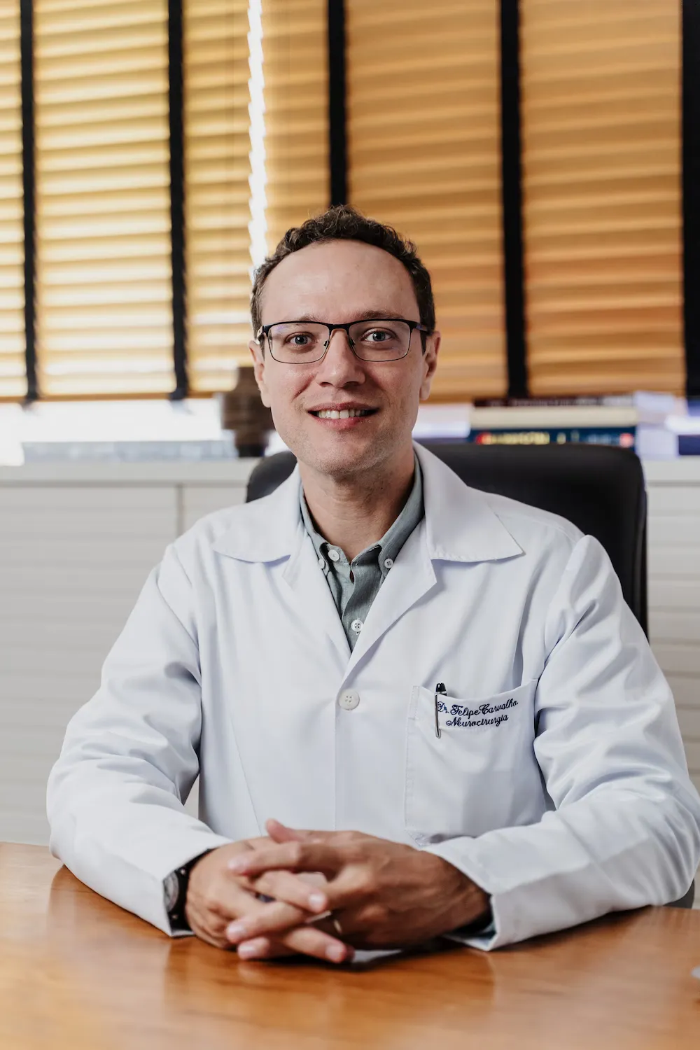 Dr. Felipe Carvalho, de jaleco, sentado à mesa do consultório