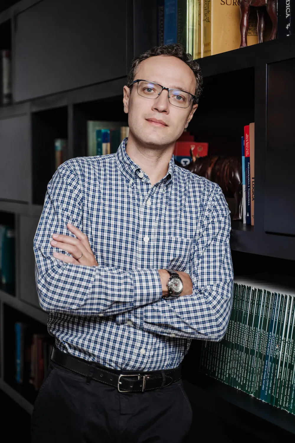 Dr. Felipe Carvalho de braços cruzados em frente a uma estante de livros