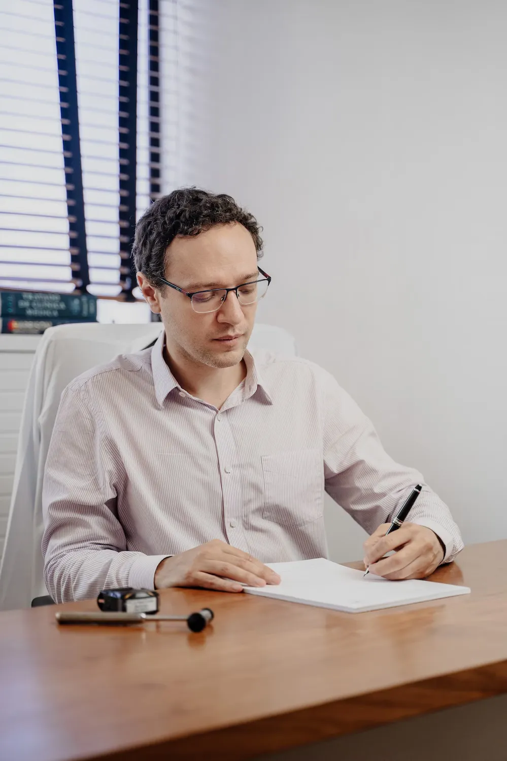 Dr. Felipe Carvalho fazendo anotações à mesa do consultório