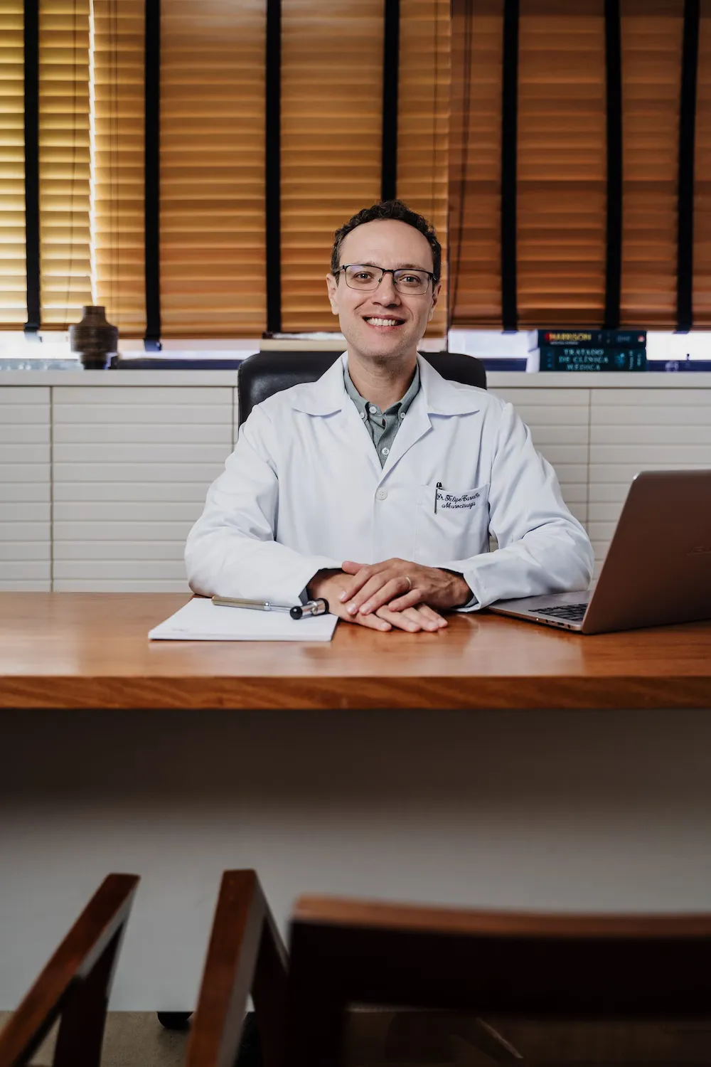 Dr. Felipe Carvalho, de jaleco, à mesa do consultório