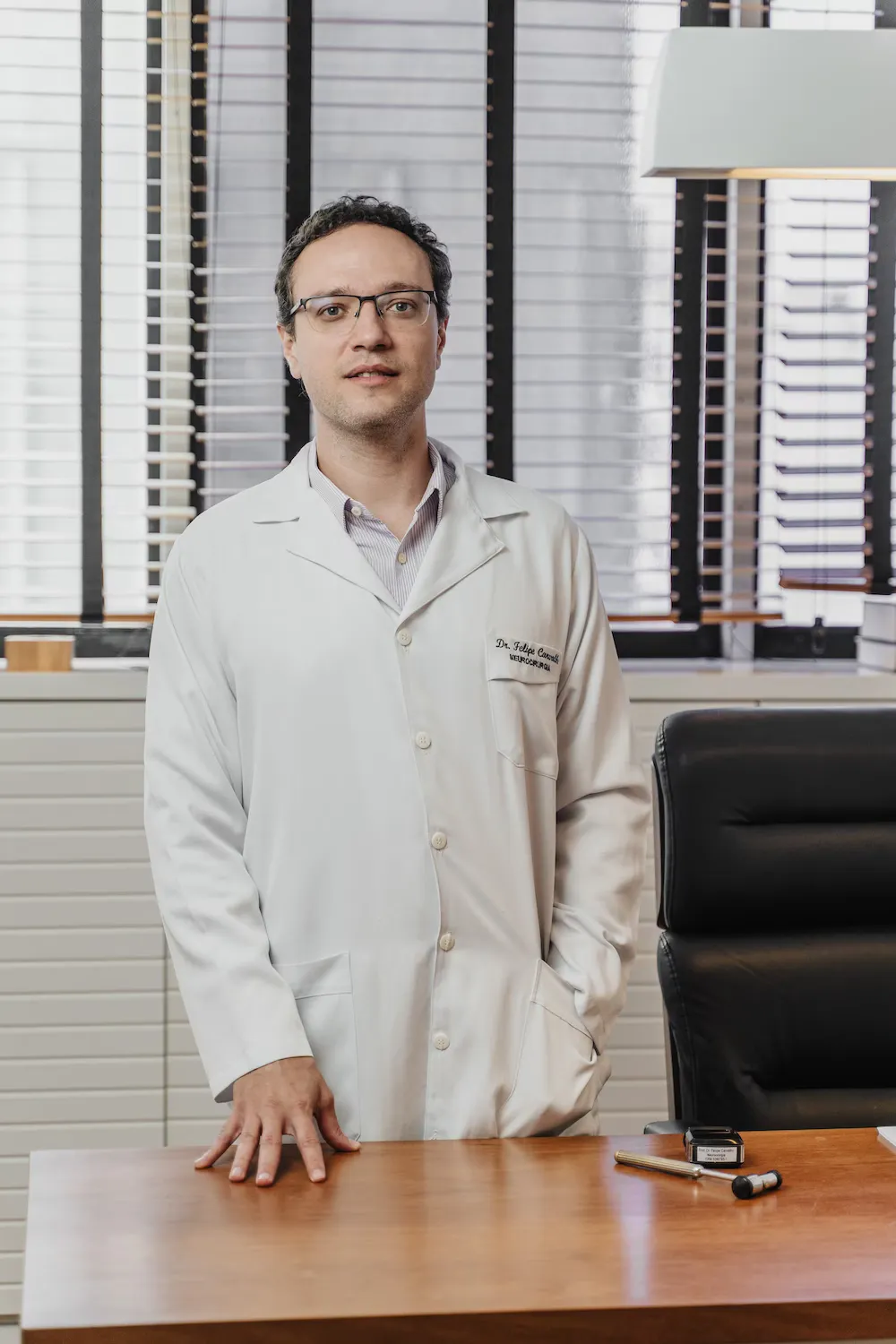 Dr. Felipe Carvalho, de jaleco, em pé no consultório